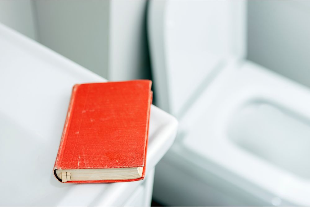 eine rotes Buch liegt auf einem Waschbecken neben einer geöffneten Toilette